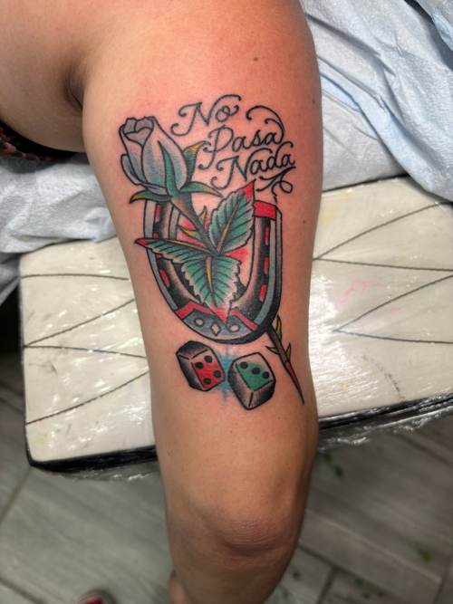 Traditional-style horseshoe and rose tattoo with the script No Pasa Nada