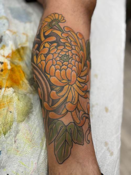 Orange and yellow chrysanthemum tattoo on a forearm