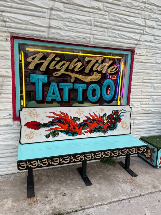 High Tide Tattoo storefront in Port Isabel with a lit High Tide Tattoo sign and a hand-painted bench