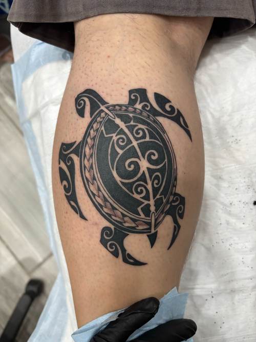 Black tribal-style sea turtle tattoo on a calf